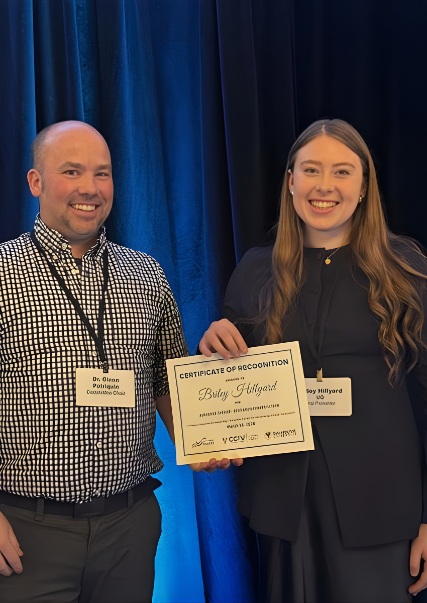 Dr. Glenn Patriquin, wearing a checkered shirt, stands next to Briley Hillyard, in all black. Both are smiling and holding the certificate for Audience Choice - Best Oral Presentation 