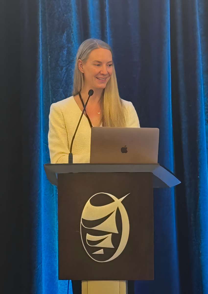Dr. Kyla Hildebrand smiles at the audience as she stands at the podium to give the keynote lecture.