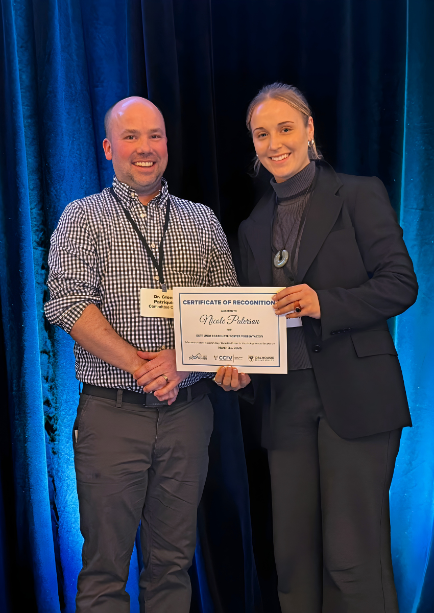 Dr. Glenn Patriquin in a checkered shirt smiles and stands next to Nicole Paterson who is wearing all black. Nicole is smiling while holding the certificate for Best Poster Presentation - Undergraduate.