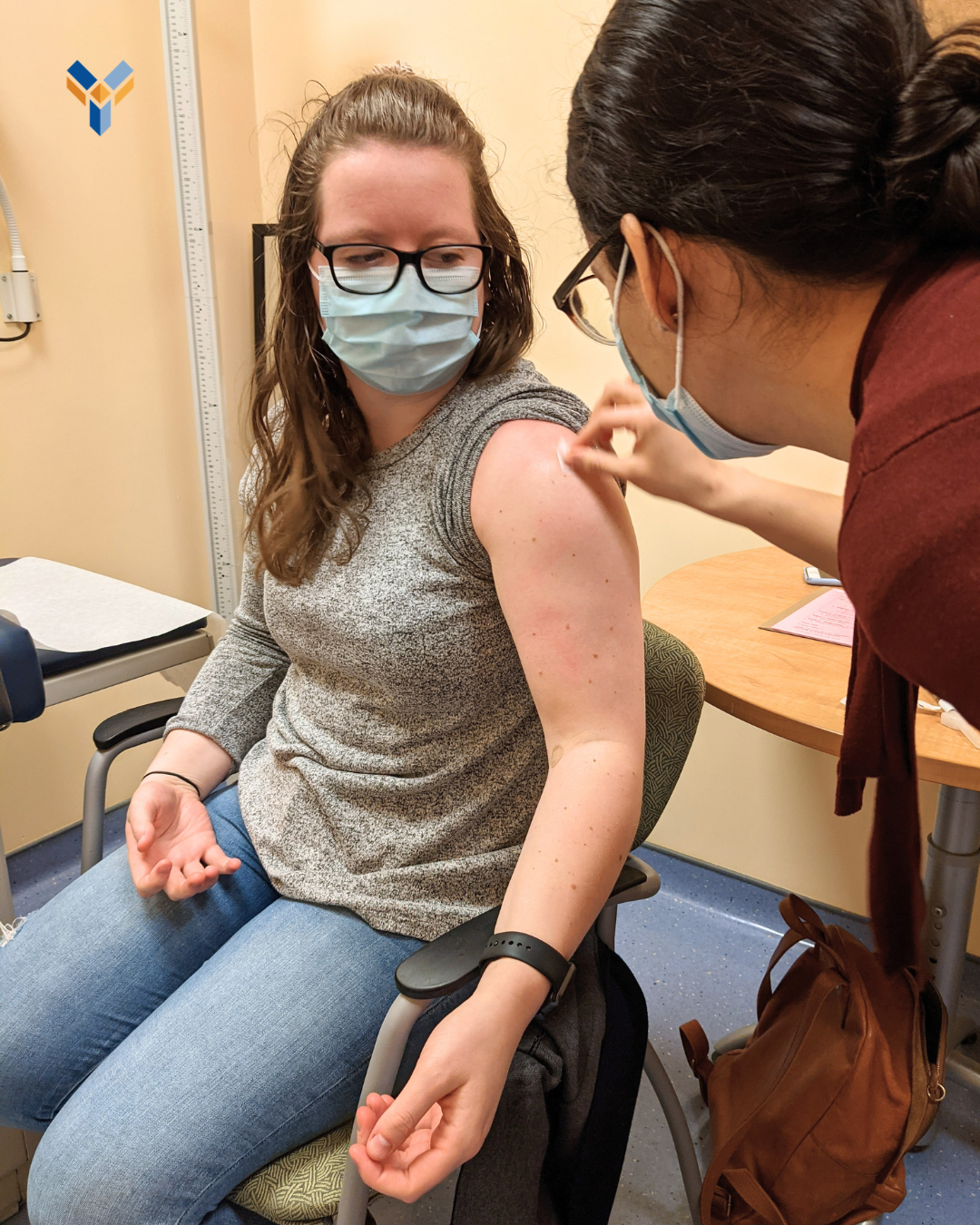 A CCfV volunteer wearing a medical mask looks on as a study staff member swabs her arm before a vaccine.