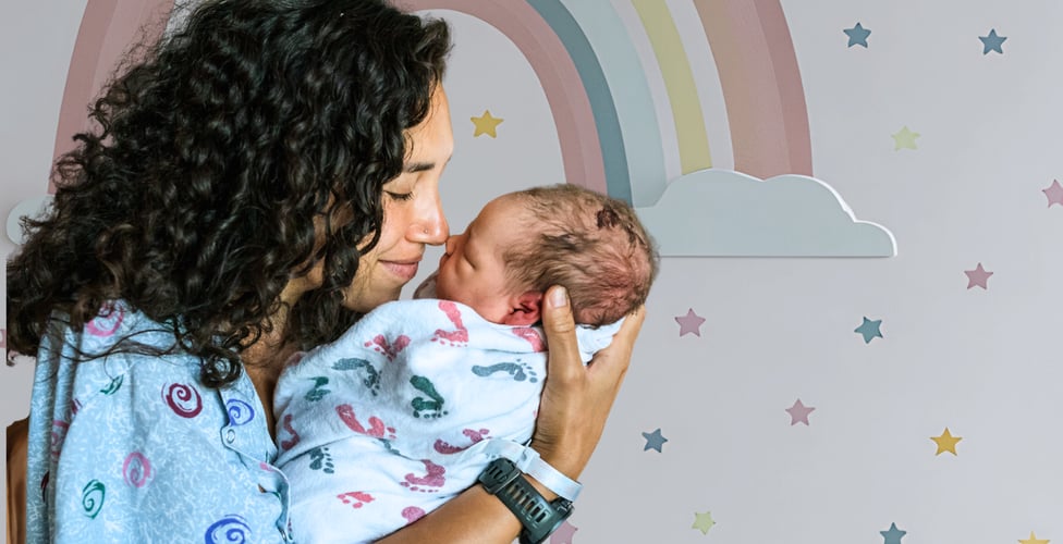 A woman with curly black hair smiles as she touches noses with her newborn infant.